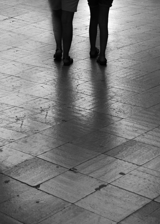 Two women walk side by side on a dark street of shiny tilesの写真素材