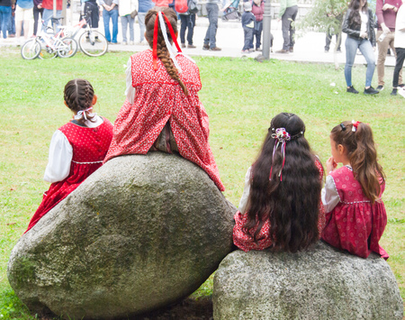 Little girls with red folk dress from the past sitting on two granite rocksの写真素材
