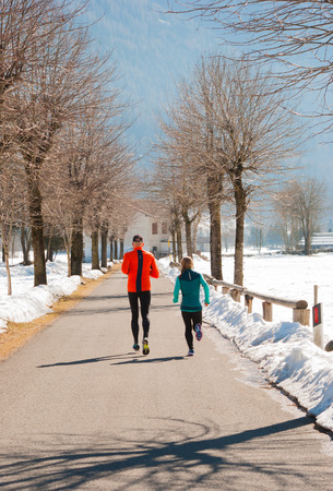 Man and woman are running on a road with snow and leafless trees aroundの写真素材