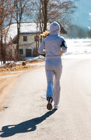 Girl running with gray tracksuit on a road with snowの写真素材