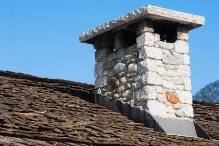 Stone chimney on roof with wooden shingles and blue sky backgroundの写真素材