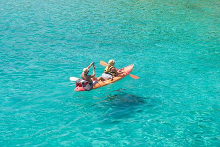 Tourists on a red canoe making photos on a beautiful turquoise seaの写真素材