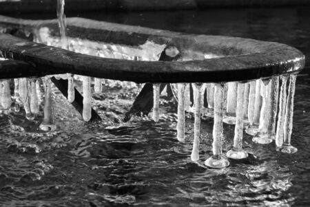 Iced water with icicles attached to a metal structure of a fountainの写真素材