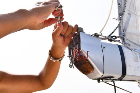 Hands with blue colored nails of a woman as she knots a rope on the main boom of the sailboatの写真素材