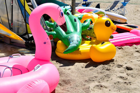 Pink swan and yellow duck and green crocodile inflatables left on the sandの写真素材