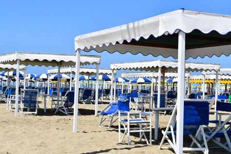 Group of well-aligned white gazebos and beach chairs on the sandy beach without peopleの写真素材