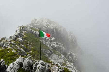 Tricolour flag fluttering over the apex of mountains partially covered by low cloudsの写真素材