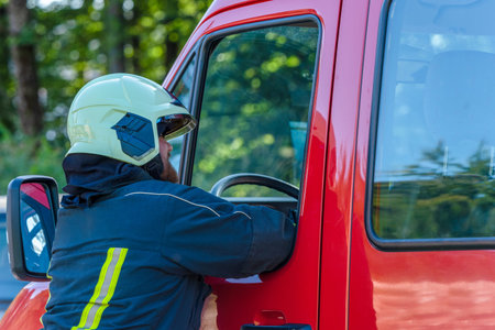 Firefighter in suit and helmet photographed from the side talking to a colleague in a fire truck
