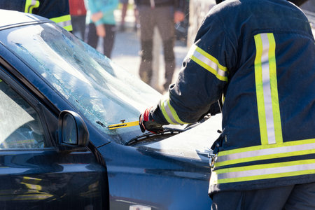 Firefighters, fire man cut a car glass in car accident.  Blurred people at the back.