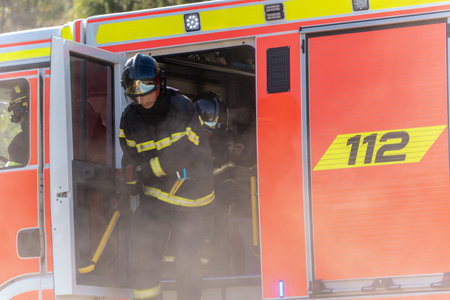 Firefighters in suit and helmet jumping out of a fire truck. Photographed the moment they arrived at...