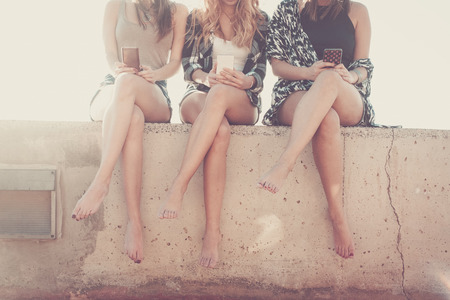 Group of women young and beautiful friends use a smartphone.. Composition with faces cutted and no visible. six legs together in friendship.の写真素材