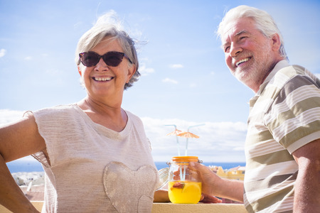 Smile old woman and man with a fruit cocktail under the sumer sun in the rooftop. Ocean view with blue and clear sky.の写真素材