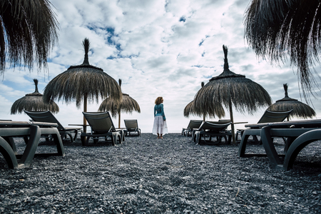 dark and blue colors and tones for epic image with beautiful caucasian middle age model at the beach in the winter weather. cold and nice dress and body stand up alone with amazing clouds backgroundの写真素材