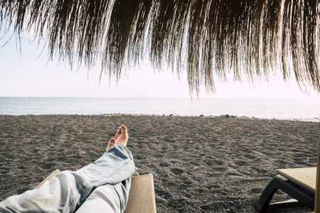 man feet point of view while alone rest and relax at the beach with waves wind and ocean in front at the end of the sand. nice leisure activity of vacation for male with jeansの写真素材
