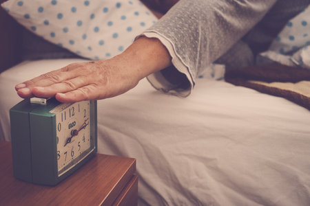 elderly woman wake up touching the alarm clockの写真素材