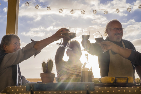 happy group of adults celebrate an event with cups of wine outdoor in the terrace with sunset and backlight. golden tones for happiness lifestyle concept. two men and two womenの写真素材