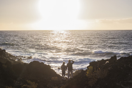 mother and son dressed in trekking admire the sea and the waves at sunsetの写真素材