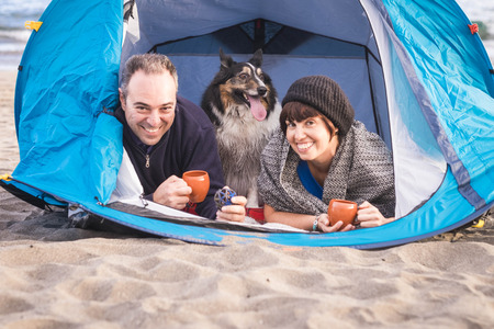 family portrait for alternative vacation time summer on the beach with a tent. nice and smile a male and a woman with a border collie dog in the middle like a son. happiness and freedom concept under the sunlightの写真素材