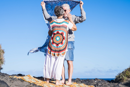 man and woman senior mature people in sweetness and carefree on the ocean coast. vacation or new life retired concept. colorful clothes and scenic place. love and life forever togetherの写真素材