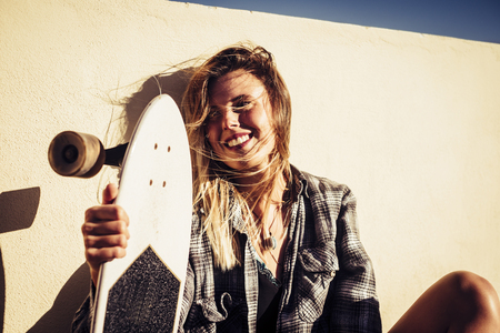 beautiful smile for a caucasian blonde young woman sitting down with a white skateboard sunny day of vacation for alternative lifestyle. wind in the hait.の写真素材
