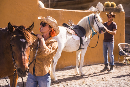 nice caucasian couple outdoor prepare and check horse equipments ready to go live a new adventure travel in aloternative way to discover a natural paths and world. country life concepts for young man and womanの写真素材