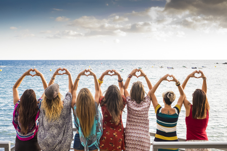 beautiful seven girls from the backside doing a heart with the hands looking at the ocean waiting the sunset in vacation leisure activity. friendshipt all together forever concept, travel to sea placesの写真素材