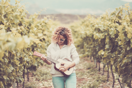 happy caucasian beautiful middle age woman walking in the vineyard playing an ukulele and singing. alternative freedom and lifestyle vacation conceptの写真素材