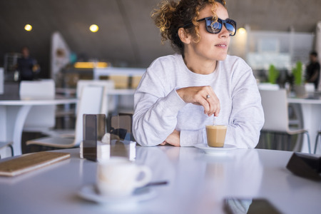beautiful caucasian middle age women with sunglasses take and drink a coffee in a bar. outdoor light from window for a leisure rest moment during the day. quiet and relaxの写真素材