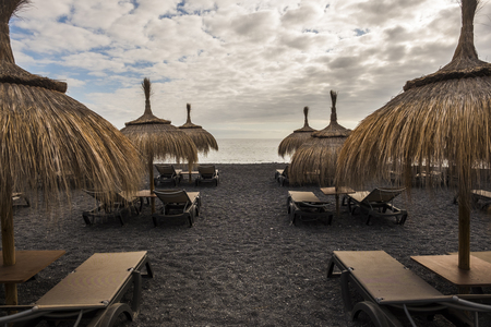 umbrellas and seats on the beach in tenerife island. place for vacation with no one there. closed time for bad weatherの写真素材