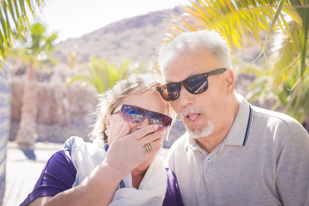 nice faces laughing for an elderly couple in vacation. Palms and sunlight and they wear sunglasses. Nice and funny life concept.の写真素材