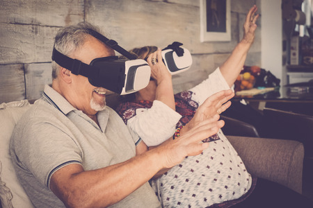 senior man and woman with goggles headset virtual reality eyeglasses playing and have fun sitting on the sofa at home.の写真素材