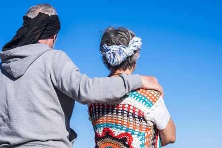 hippy and colored couple of adult senior touch together with love and romantic hug looking at the blue sky. life alternative forever conceptの写真素材