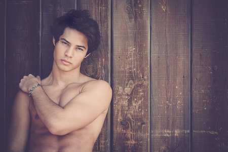 Young black hair beautiful man with no t-shirts and nice body. Black hair with one hand on his shouder he looks at the camera. Wooden backgroundの写真素材