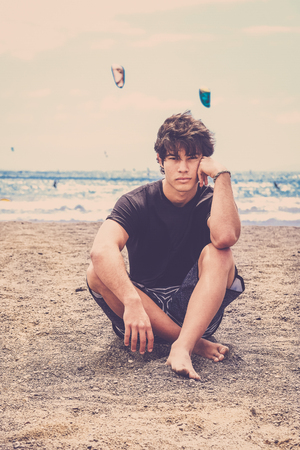 Sit down nice guy with black t-shirt on the beach of Tenerife. Blue ocean and waves behind, warm vintage filter. Look at the camera.の写真素材
