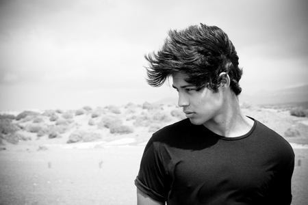 Beautiful young boy on the right of the image with wind on the hait. Moving black hair over a nice face. Desert black and white in background.の写真素材