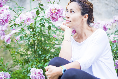 Beautiful wooman 40 years old look at her side thinking happy. Roses flower background. Nature outdoor colors.の写真素材