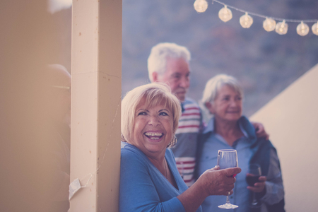 big smile for aged woman during leisure on the terrace by night. Drinking some wine and having fun at party with friends seniorの写真素材