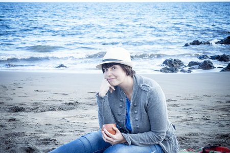 nice beautiful young lady smiling with hat sitting down at the beach in winter. vacation nice leisure concept outdoor.の写真素材