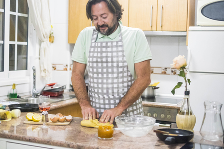 man with beard and apron preparing dough for cake in his home kitchen with glass of wine.の写真素材