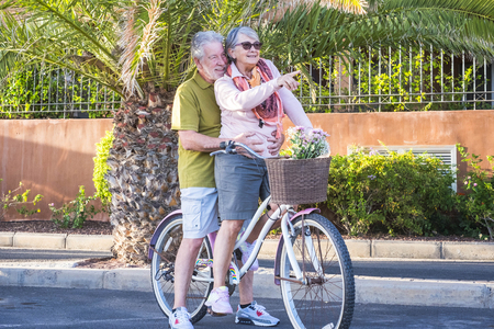 senior couple in love leisure outdoor together on a bike vintage style smiling and having fun under the sun of vacation. alternative way to be retired living in a tropical placeの写真素材