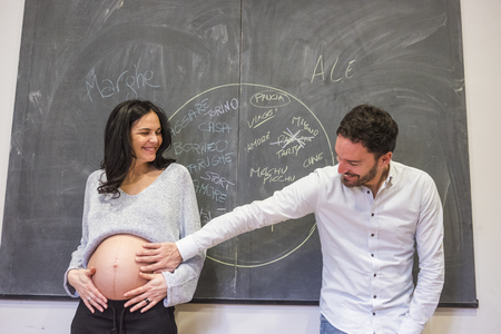 couple man and pregnant woman beautiful models joking lifestyle in front of a black wall full of positive notes and projects for their future family lifestyle. indoor romantic and funny conceptの写真素材