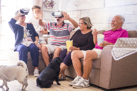 big family leisure at home with virtual reality games goggles headset modern technlogy for new experience. adult matures grandfathers and teenager nephew have fun with two pug dogsの写真素材