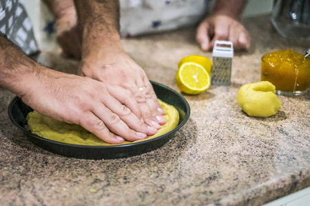 Hands arrange dough for dessert in the baking pan before spreading the jam.の写真素材