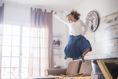 crazy happiness for beautiful woman jumping at home for great joy after a success or for a nice lifestyle. hippy chic bohemien clothes and bright funny image with winner conceptの写真素材