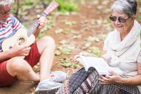 beautiful caucasian couple of adult senior 70 years old enjoy the time in the summer playing an ukulele together in the vineyard. outdoor countryside happy people conceptの写真素材