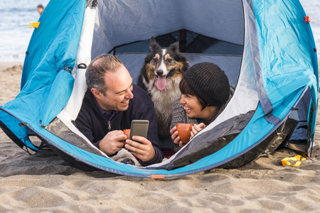 nice people with cute puppy inside a cell phone to send message or take picture. beach camping freedom alternative vacation in tenerife with your best friends dogの写真素材