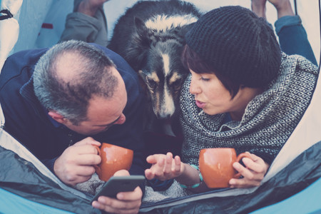 nice people with cute puppy inside a cell phone to send message or take picture. beach camping freedom alternative vacation in tenerife with your best friends dogの写真素材