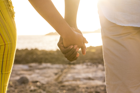 couple of black race african hands touch and take them in a love forever together concept. timeless life outdoor at the beach with sunset backlight and ocean in background. summer time and lifestyleの写真素材