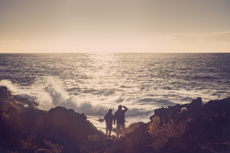 mother and son dressed in trekking admire the sea and the waves at sunsetの写真素材