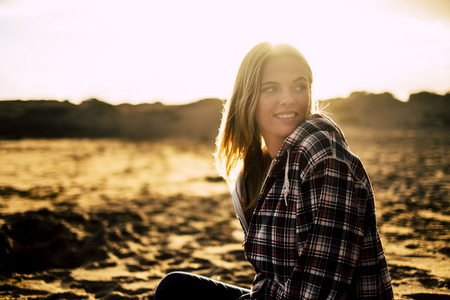 sun backlight and sensual portrait of beautiful young blonde female on the sand at the beach. focus on hair moved by the windの写真素材
